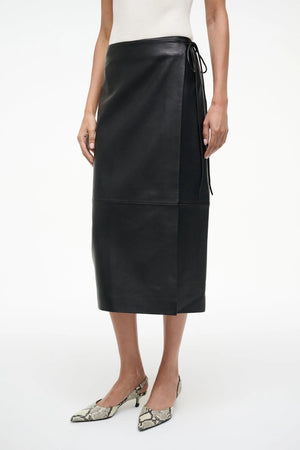 Model wearing the Roman Leather Wrap Skirt in Black by Staud, demonstrating its versatile style.