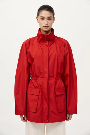St. Agni Paper Taffeta Parka in Red displayed on a table, emphasizing its lightweight composition of 80% recycled polyester.