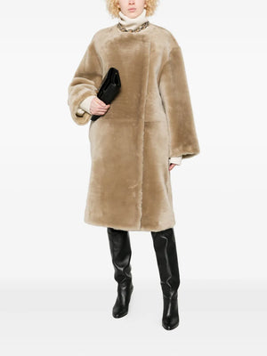 Detail shot of the collarless shearling coat in rye by TOTEME, featuring a hook-fastened, double-breasted front and elegant slip pockets.