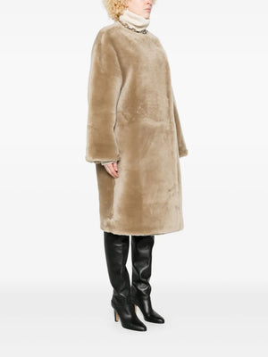 The collarless shearling coat in rye on a model, highlighting its knee-length hem and pairing with high boots, perfect for stylish fall outfits.