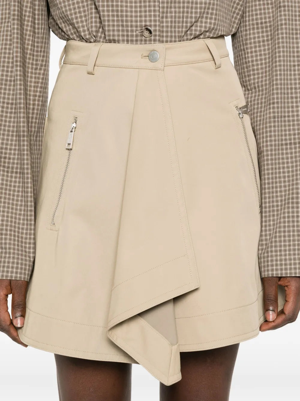 Side view of the Inge Mini Skirt in Beige by Nanushka, featuring zippered pockets and flowing design.