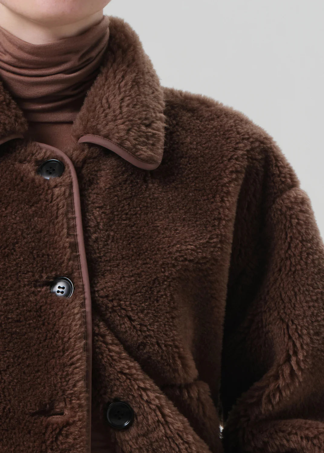 The Astrid Sherpa Jacket in Warm Tan draped elegantly on a hanger, emphasizing its fine details.