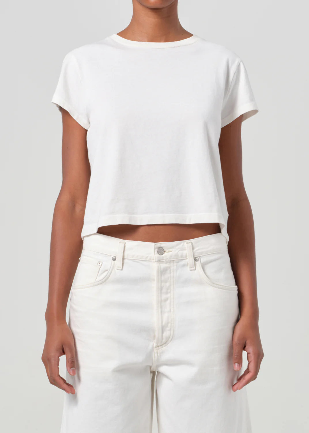 Model wearing Agolde Adine Shrunken Tee in White Ash, paired with denim shorts for a chic look.