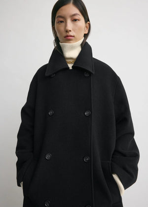 Model wearing the Shield Coat in Black by TOTEME, styled with the collar up for extra warmth.