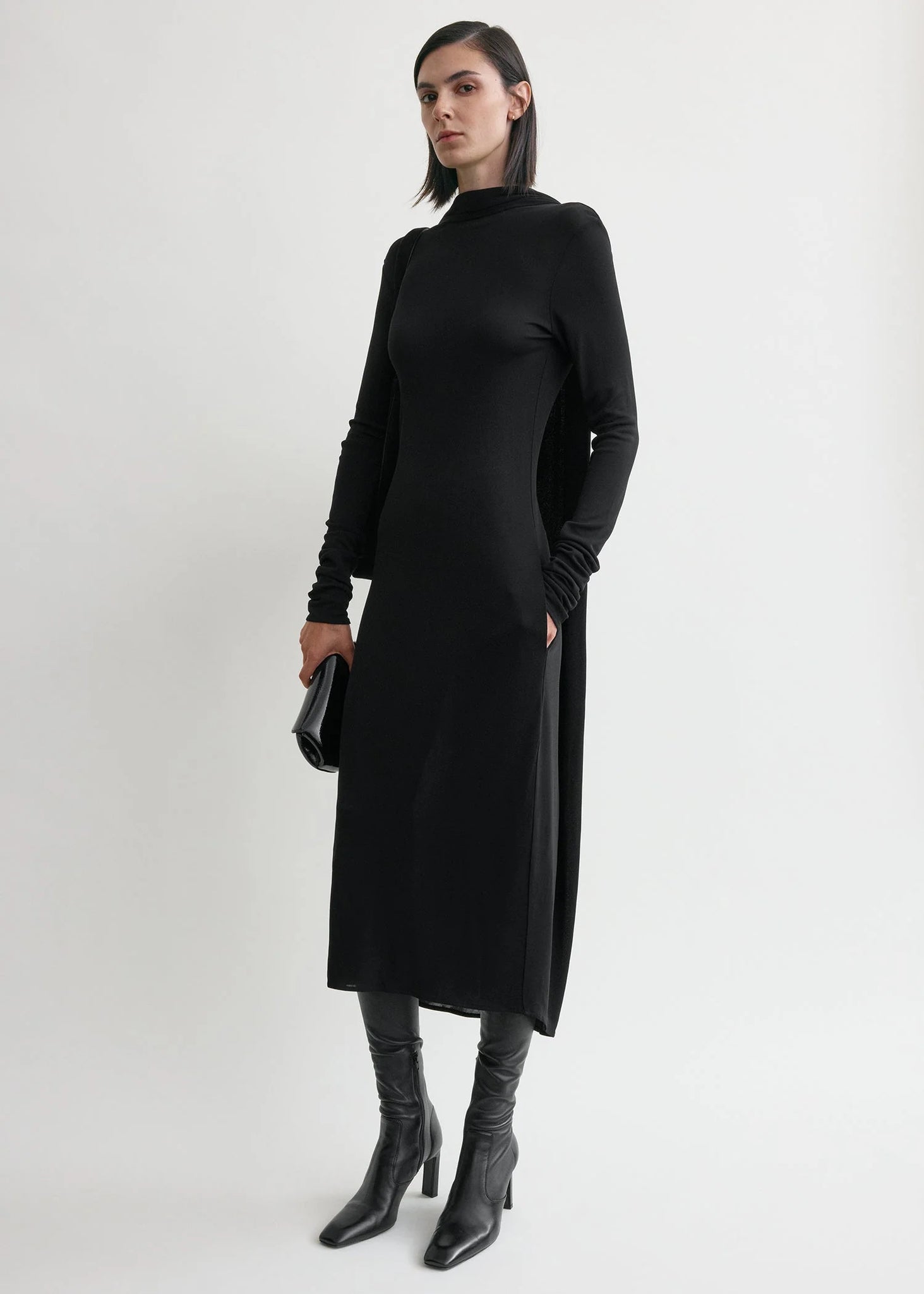 Model wearing Cocoon Cape Dress in Black by TOTEME, highlighting its relaxed cocoon shape and slightly dipped hem.