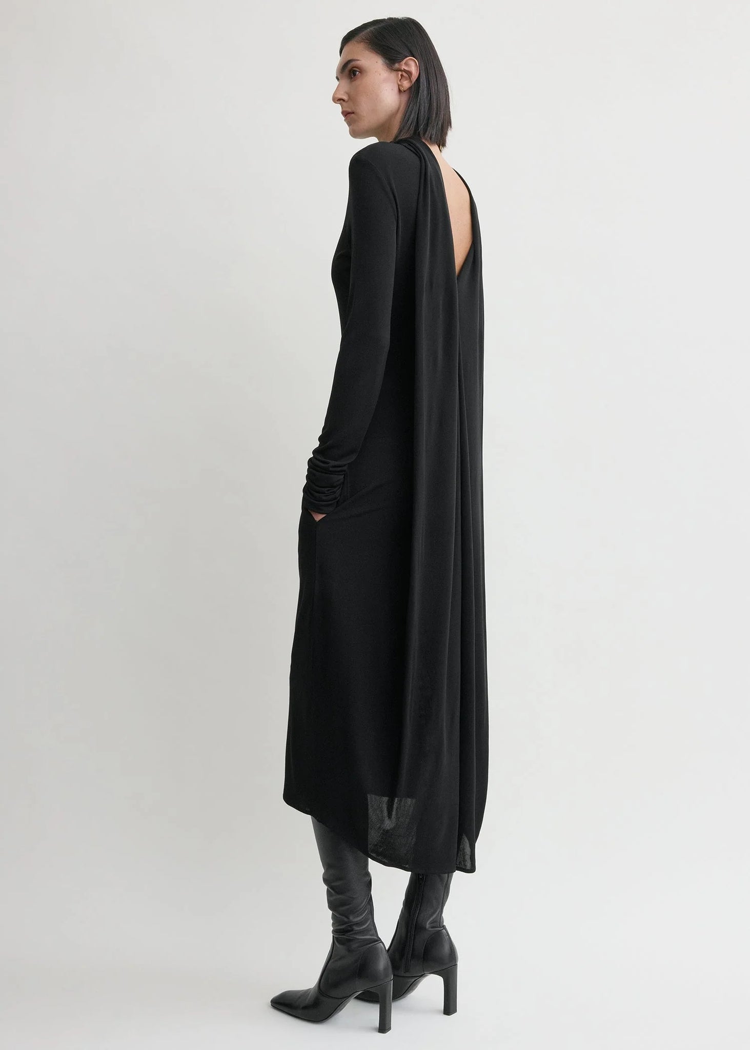 Side view of the Cocoon Cape Dress in Black by TOTEME, emphasizing the long sleeves and exquisite back design.