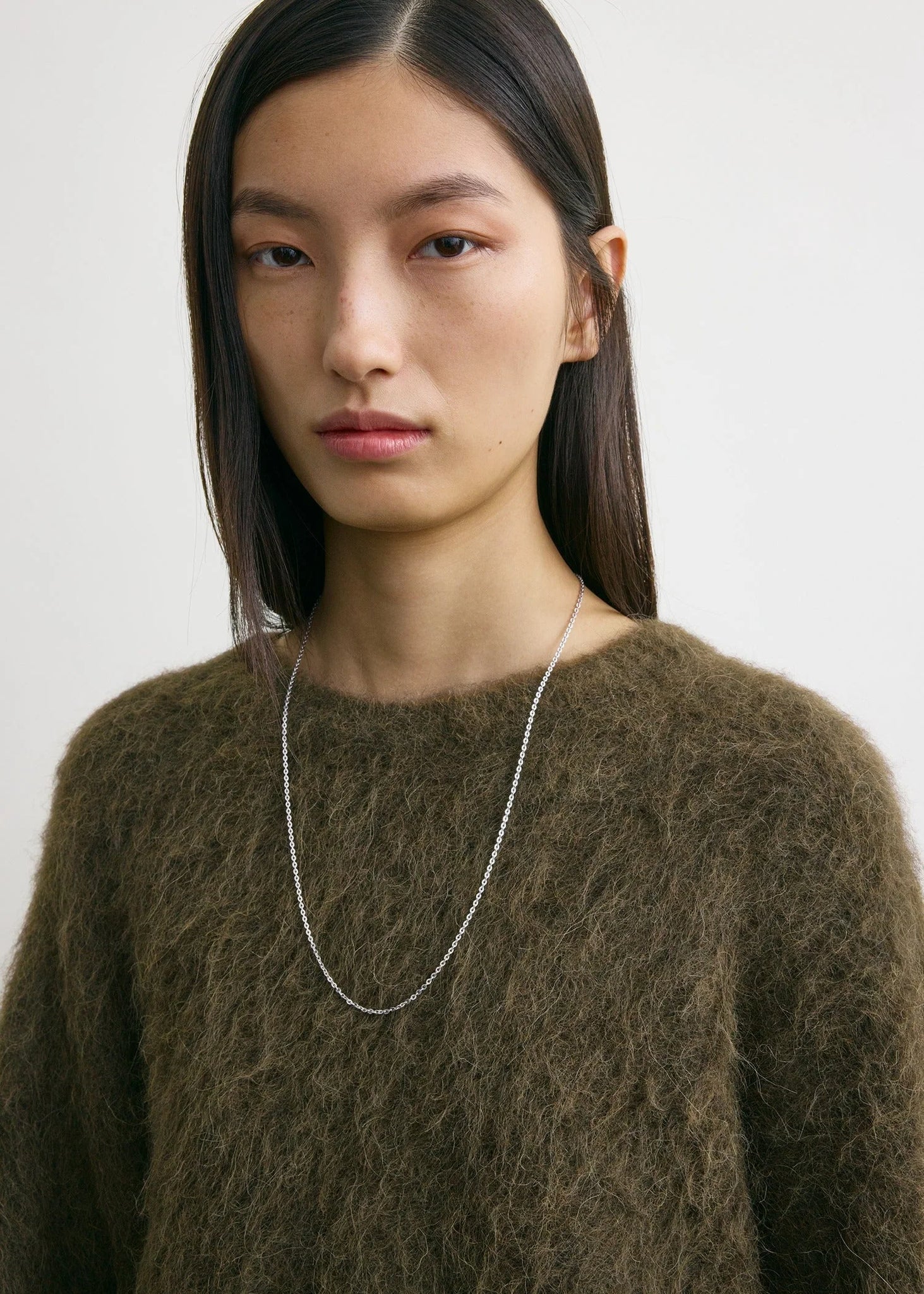 The Boxy Alpaca Knit in Pepper by TOTEME displayed on a hanger, showing its oversized fit and trendy design.