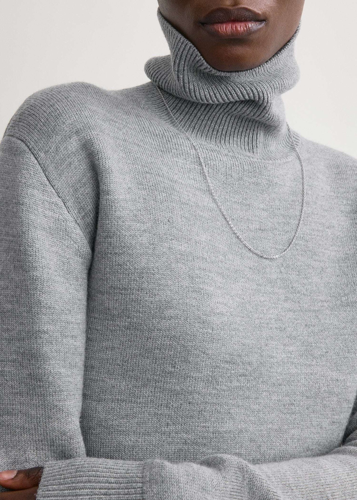 Back view of the High-neck Double Knit Sweater in Pale Grey Melange, emphasizing the long, sculptural hem.