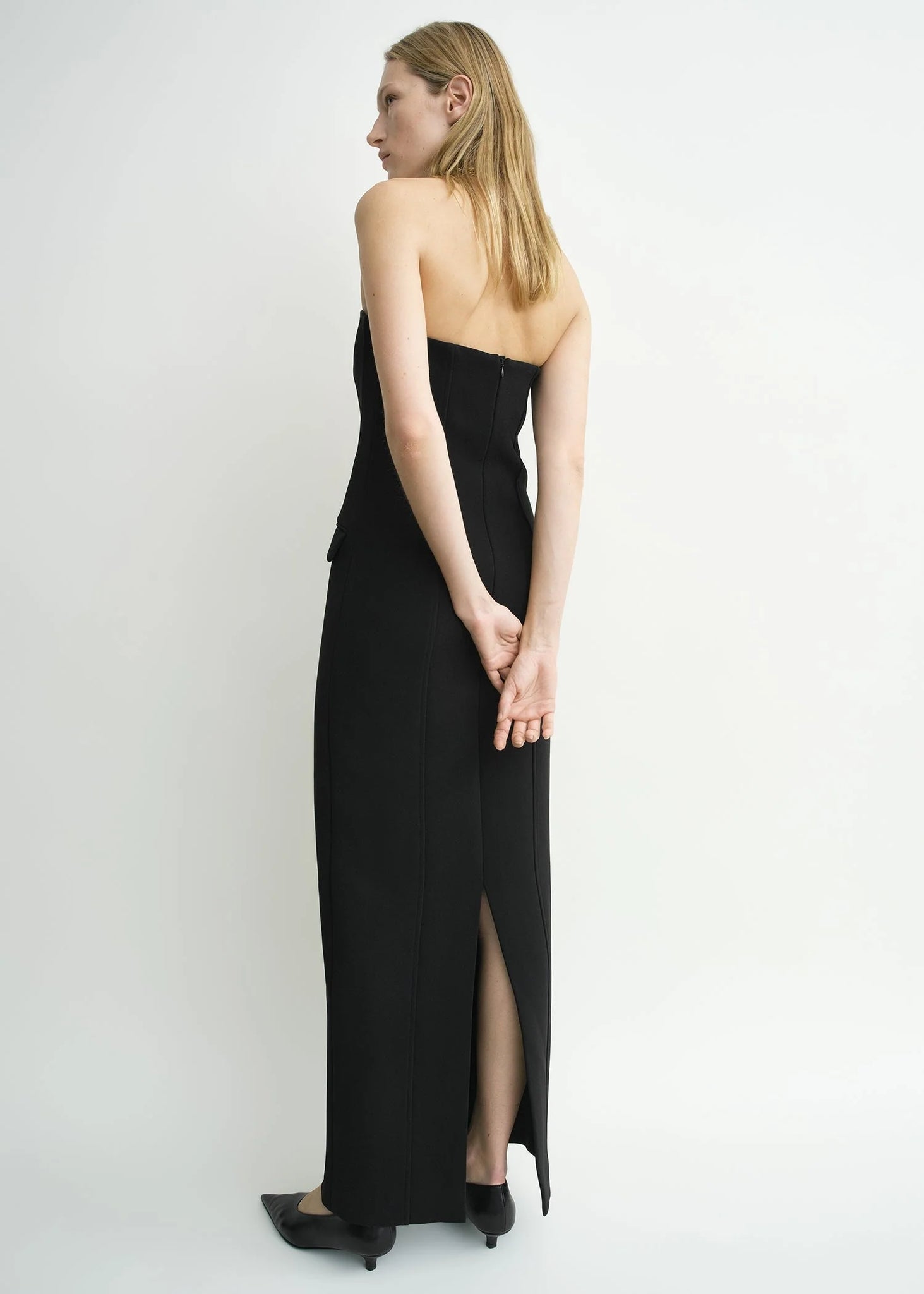 Side profile of the TOTEME Strapless Pocket Dress in Black showing its tailored darted construction.
