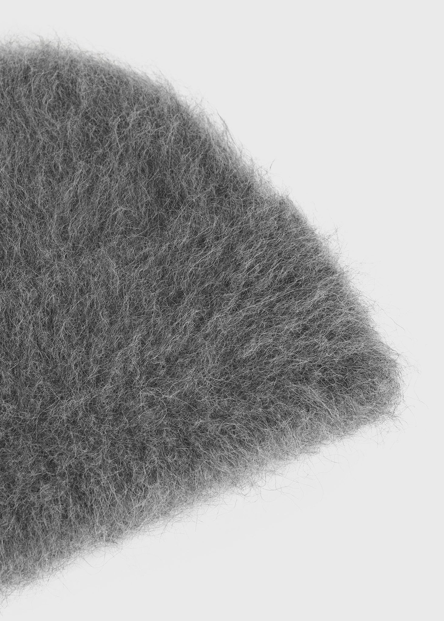 Alpaca Beanie Hat in Dark Grey Melange laid flat on a surface, emphasizing its rich color and luxurious feel made from alpaca wool by TOTEME.